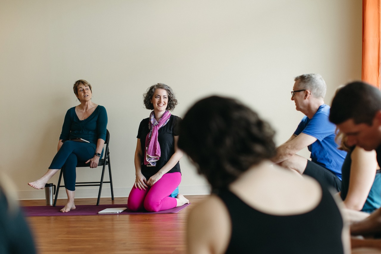 Scene from yoga teacher training. The group sits in a circle smiling.