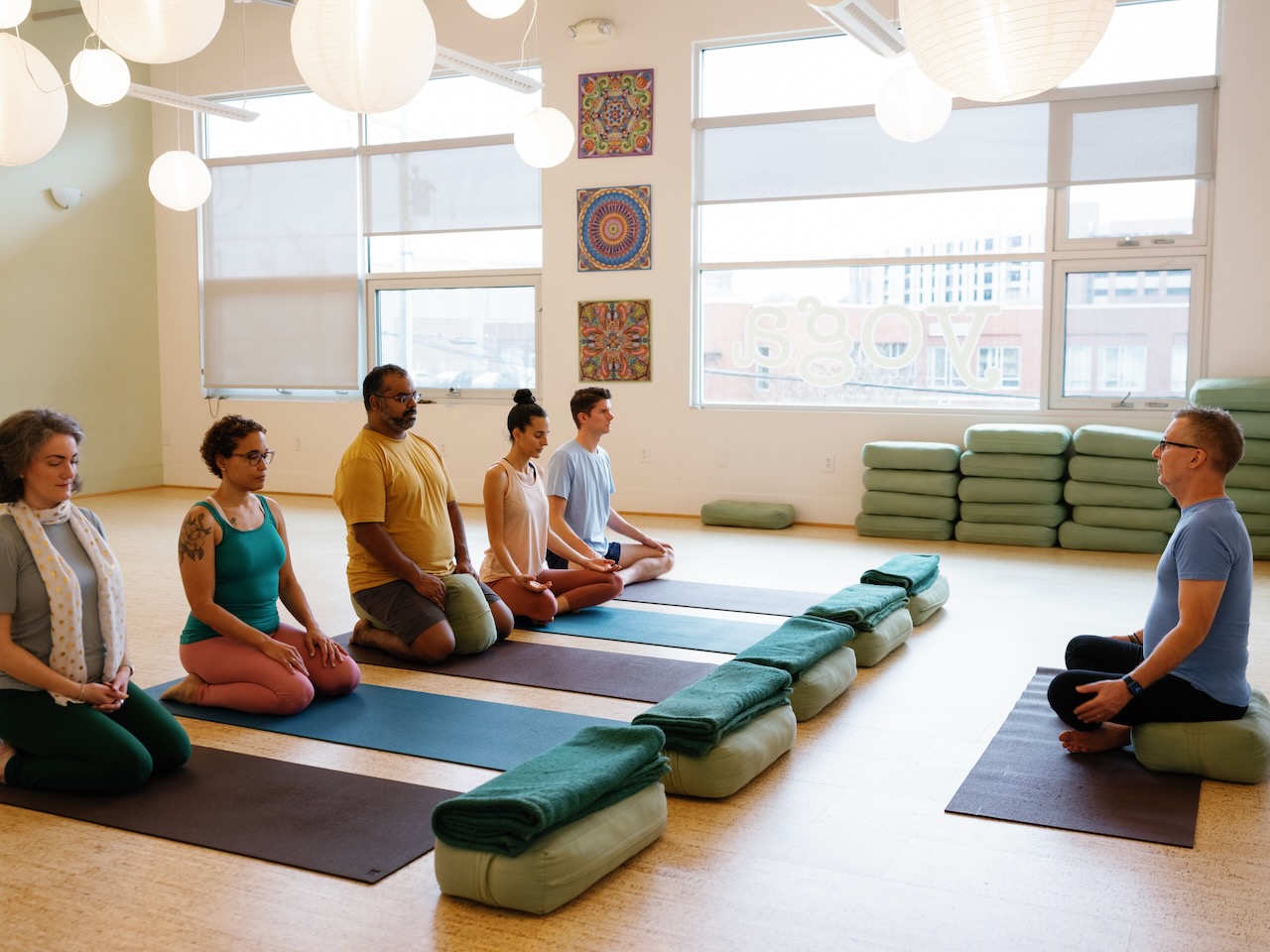 Students sit in centering in a sunny yoga studio