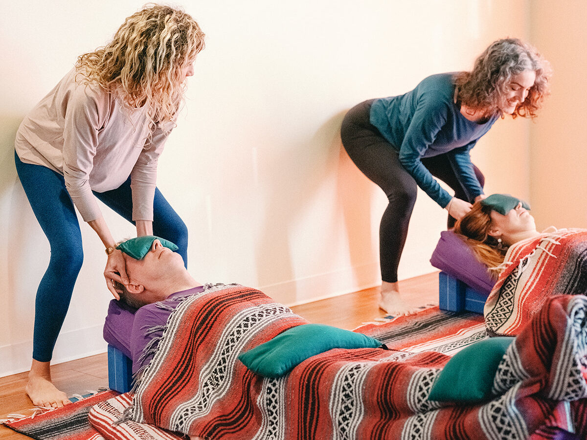 Alexandra DeSiato and Sage Rountree help yoga students relax in a restorative pose