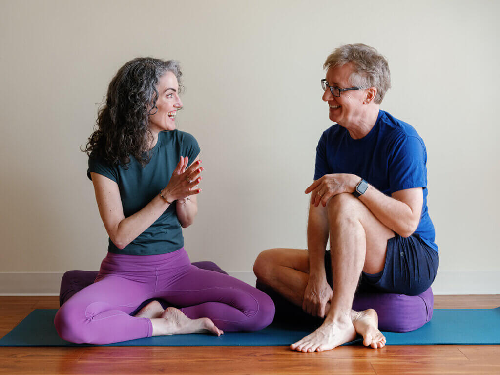 A yoga teacher and student in a one-on-one private yoga lesson, sitting together on yoga mats