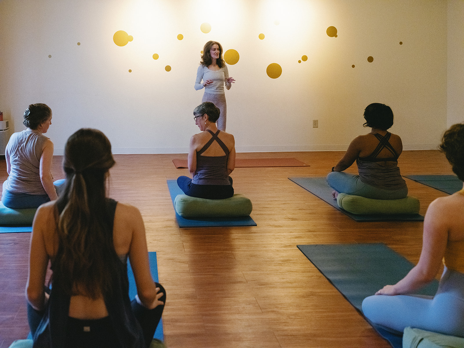 Sage Rountree stands at the front of a bright studio, teaching students seated on bolsters