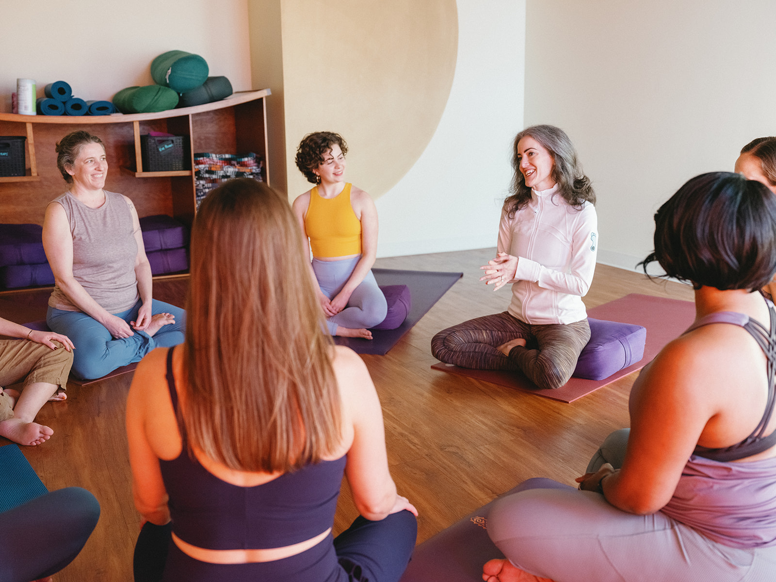 Sage Rountree talks with a circle of yoga teacher trainees seated on their mats